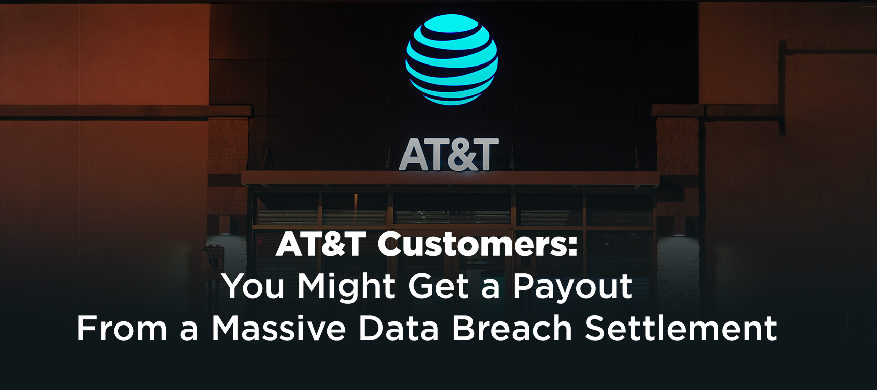 Nighttime photo of the front of an AT&T retail store, with the large, glowing AT&T blue globe logo centered at the top of the building facade. Below the logo is the word ‘AT&T’ in white capital letters. The building exterior is made of brick and concrete in warm brown tones, with a glass storefront showing some interior lights. Overlaid at the bottom of the image is bold white text that reads: ‘AT&T Customers: You Might Get a Payout From a Massive Data Breach Settlement.’ The image warns AT&T customers about a potential compensation payment resulting from a major data breach lawsuit settlement.